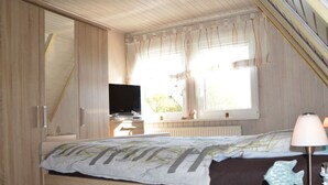 Une chambre à coucher avec un lit, une télévision, une fenêtre avec des rideaux, un radiateur et une lampe.