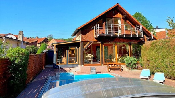 Une maison à deux étages dotée d’un balcon, d’une piscine et d’un patio aménagé avec des chaises longues.