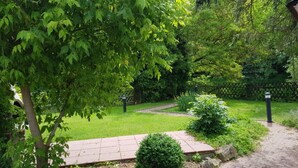 Un chemin de jardin bordé de briques, entouré d’une végétation luxuriante et d’arbres.