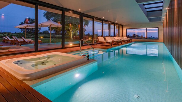 A modern indoor swimming pool with a hot tub, lounge chairs, and large windows offering views of the outdoors. - Luxury Villa sea View (Porec)
