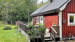 A red wooden cabin with a porch, a chimney, and a bicycle parked outside.