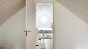 A narrow attic bedroom with a sloped ceiling, a single bed, and a small bedside table.