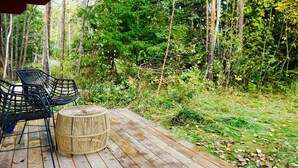 A wooden deck with two black metal chairs and a woven stool.