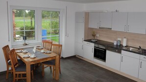 Une cuisine moderne avec des meubles blancs, un plan de travail noir et un coin repas comprenant une table et des chaises en bois.