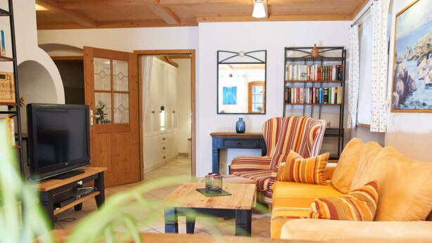 A cozy living room with a television, striped armchair, sofa, and bookshelf.