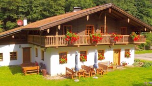 A traditional chalet with a balcony adorned with red flowers, wooden benches, and a small outdoor seating area.