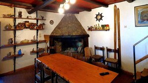 A rustic interior with a wooden table, chairs, shelves with pottery, a stone fireplace, and a wooden ceiling. - Belvilla by OYO La Baita (Polino)