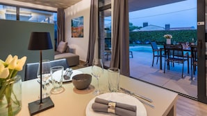 A dining area with a table set for two, a sofa, and a view of the outdoor patio. - Belexo - Luxury Home Istria (Porec)