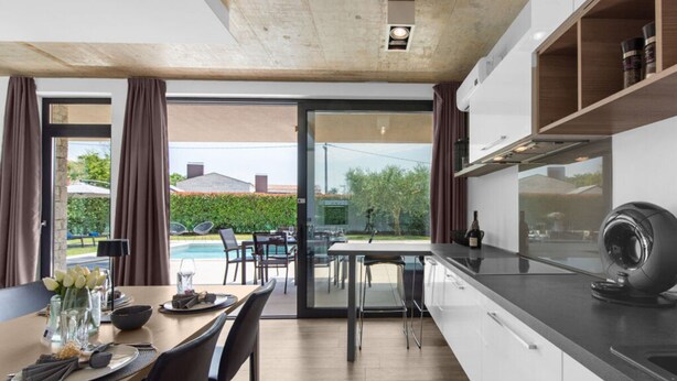 A modern kitchen with a dining area, large windows, and a view of the outdoors. - Belexo - Luxury Home Istria (Porec)