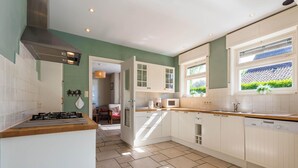 A modern kitchen with white cabinetry, a gas stove, and a window with a view of greenery. - Villa in St-idesbald Near Ster der Zee Beach (Koksijde)