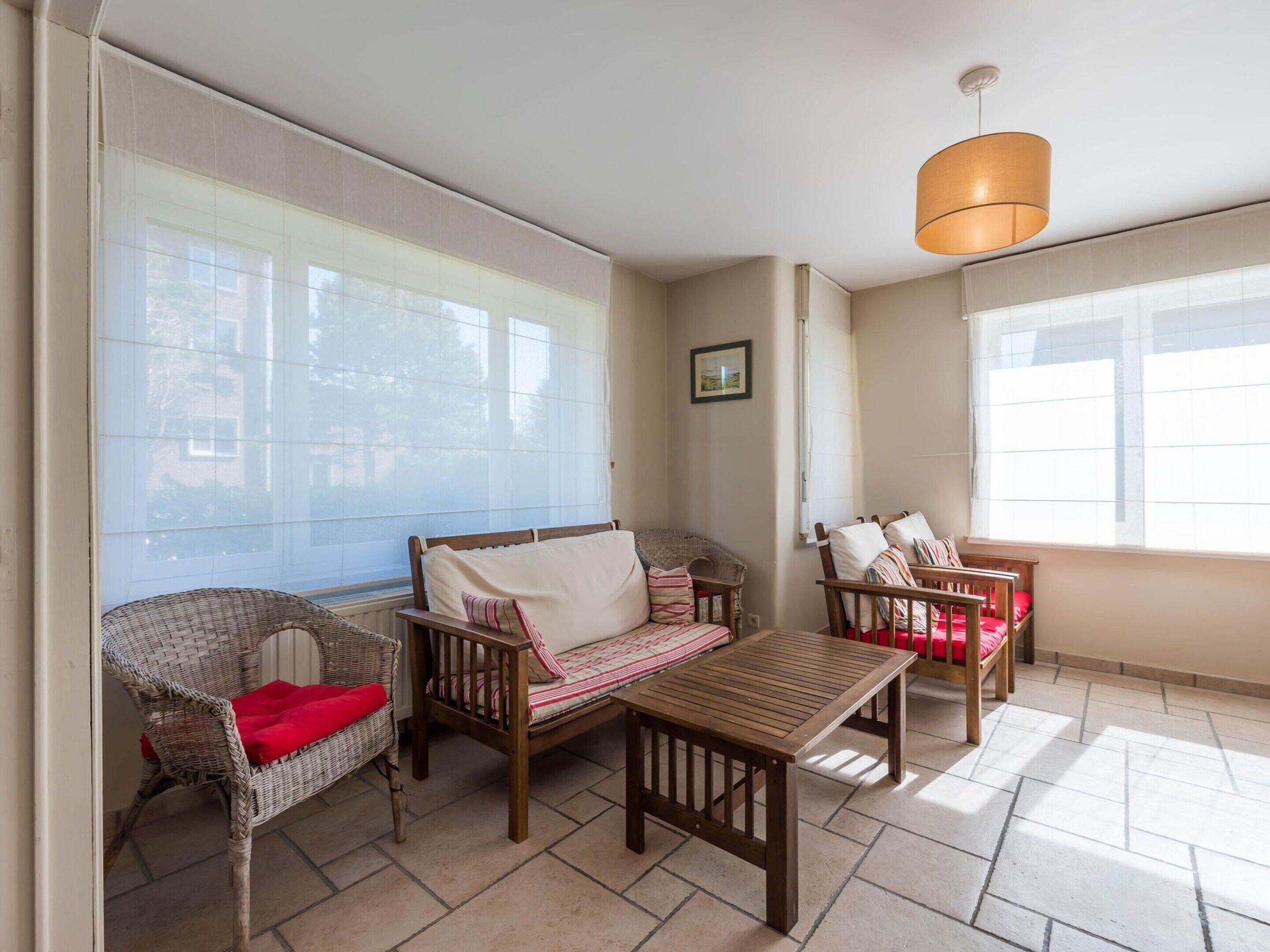 A sunlit room with a wooden table, wicker chairs, and a sofa.