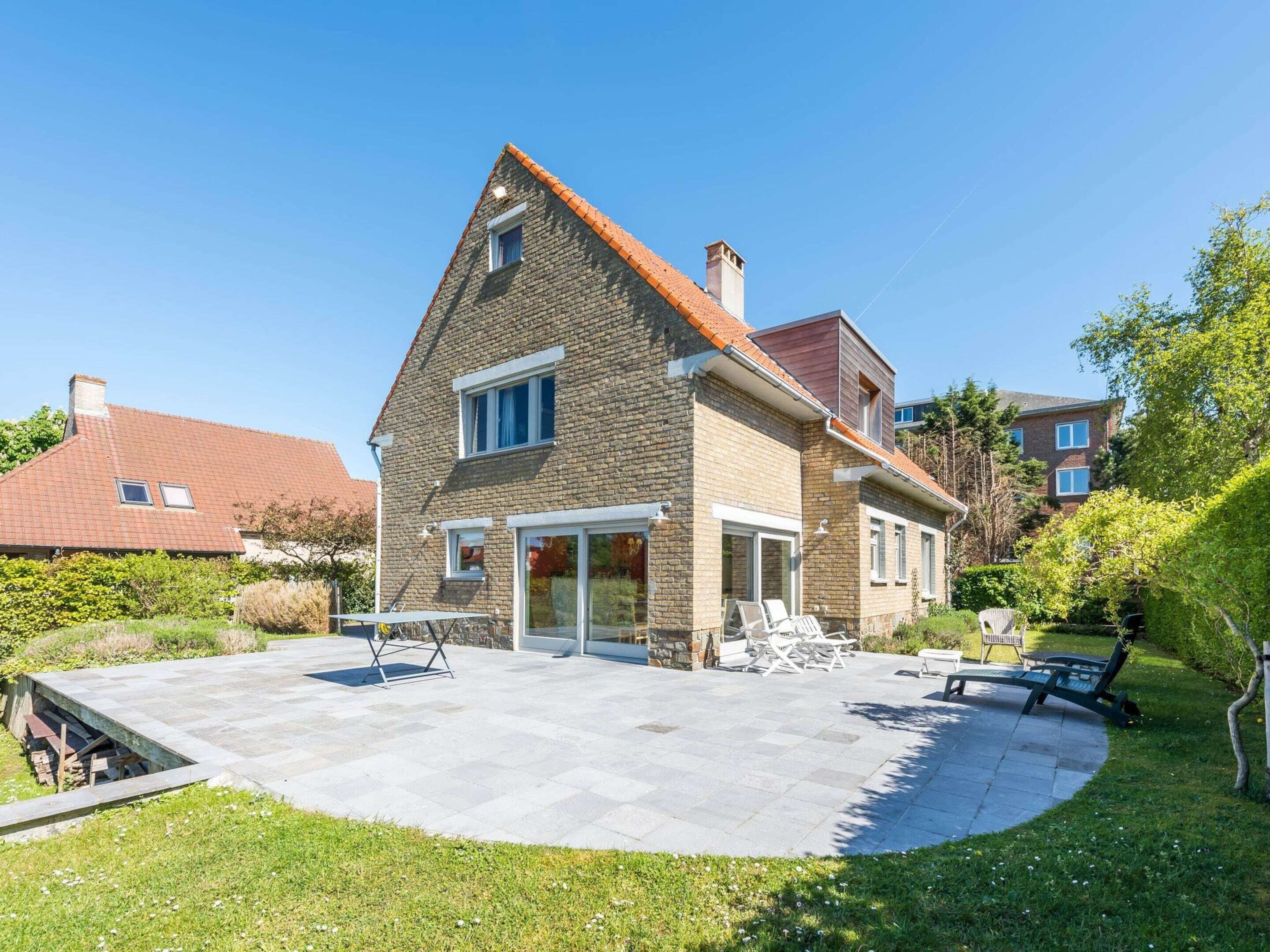 Ein zweistöckiges Haus mit Steinverkleidung, einem Ziegeldach und einer überdachten Terrasse mit Gartenmöbeln.