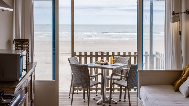 A room with a balcony overlooking the beach, furnished with wicker chairs and a table, and a bed with a white headboard. - Beach House in Wijk aan Zee With Sea View (Wijk aan Zee)