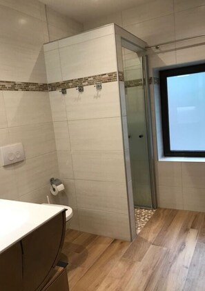 A bathroom with a shower, toilet, and a window.