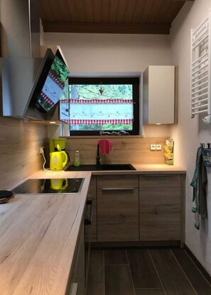 A modern kitchen with a built-in stove, a window with a view of greenery, and wooden cabinets. - Alpine Hut Hannah Comfortable Vacation Home (Hermagor-Pressegger See)