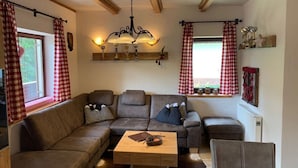 A cozy living room with a sectional sofa, a wooden coffee table, and a chandelier. - Alpine Hut Hannah Comfortable Vacation Home (Hermagor-Pressegger See)