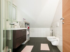 Ein modernes Badezimmer mit Duschabtrennung aus Glas, dunklem Holzschrank, weißen Fliesen und einer Holztür.