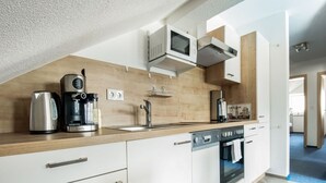 Una cuina moderna amb armaris blancs, un búllet d'acer inoxidable, una cafetera, un microones i un rentaplats.