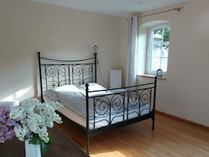 A bedroom with a metal bed frame, a bedside table with a vase of flowers, and a window with curtains. - Zonnehof in het Geiseltal (Mücheln (Geiseltal))