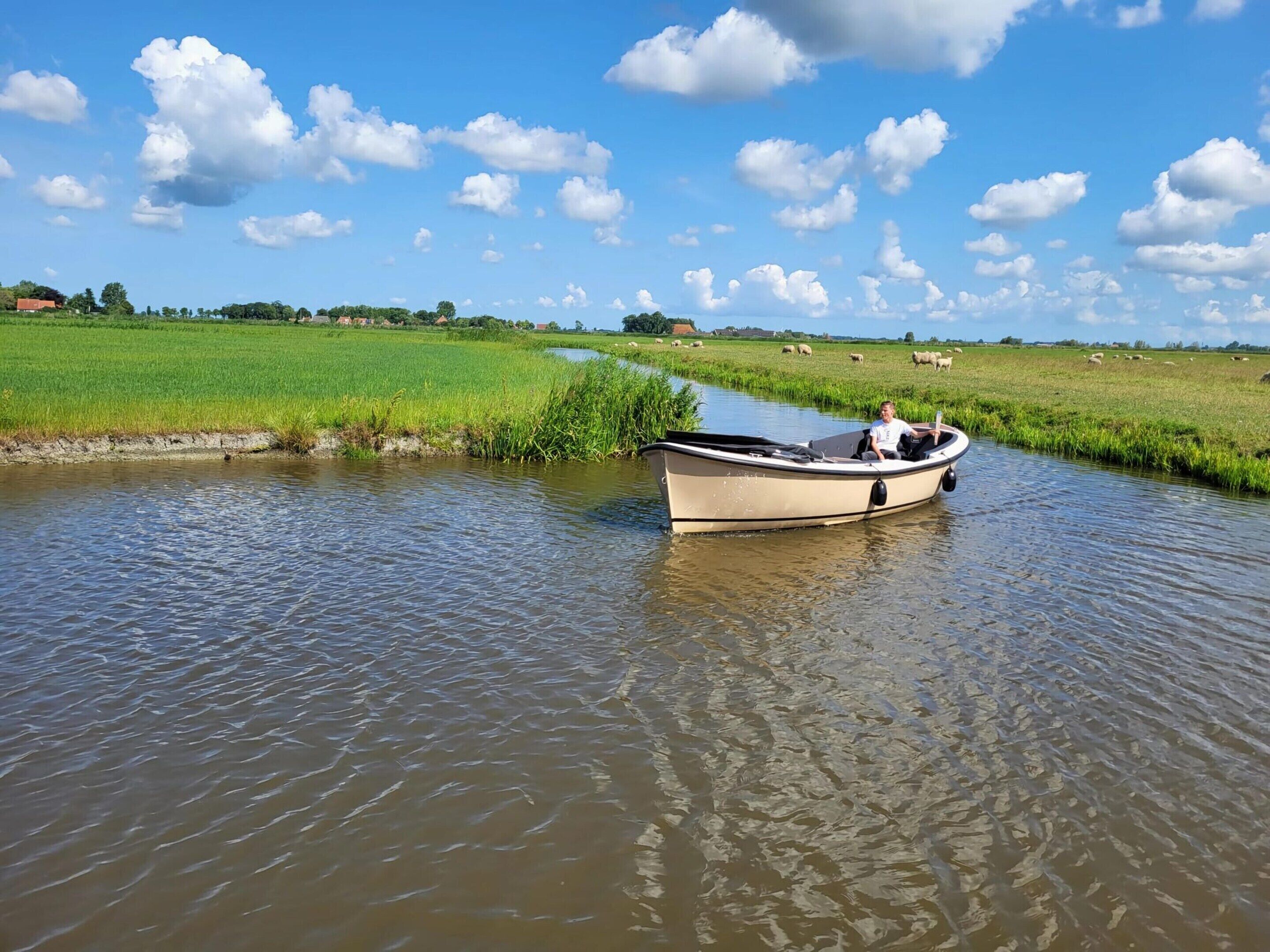 A boat on a calm river with a green landscape and scattered clouds in the sky.