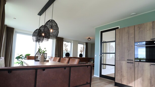 A modern kitchen with wooden cabinets, a dining area with a brown sofa, and pendant lights. - Villa in Leons With Frisian Charm (Leons)