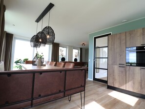 Una cocina moderna con armarios de madera, una zona de comedor con un sofá marrón y lámparas colgantes.