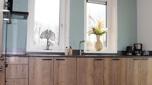 A modern kitchen with wooden cabinets, a black countertop, a window with a decorative leaf, and a potted plant. - Villa in Leons With Frisian Charm (Leons)