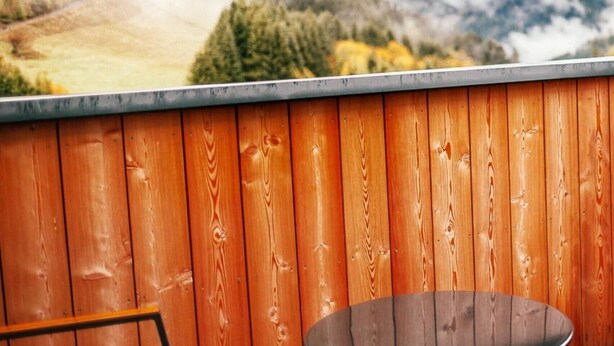 A wooden deck with a metal table and chairs, overlooking a mountainous landscape with trees and a cloudy sky. - Apartment in Hohentauern With Sauna (Hohentauern)