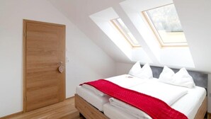 A bedroom with a wooden door, a bed with white bedding and a red blanket, and skylights. - Apartment in Hohentauern With Sauna (Hohentauern)