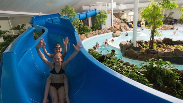 An indoor water park with a blue water slide, a pool area with rocks and plants, and people enjoying the facilities. - Beautiful Holiday Home With Luxury Bbq, in Limburg (Roggel)