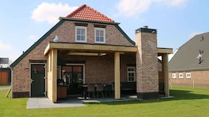 A brick house with a covered patio, a chimney, and a small attached garage. - Beautiful Holiday Home With Luxury Bbq, in Limburg (Roggel)
