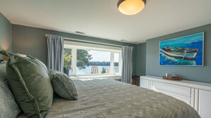 A bedroom with a bed, a painting of a boat, and a view through a window.