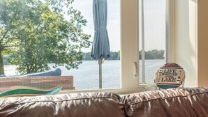 A view from a window with a lake, a blue umbrella, and a sign that says "Life is better at the lake."