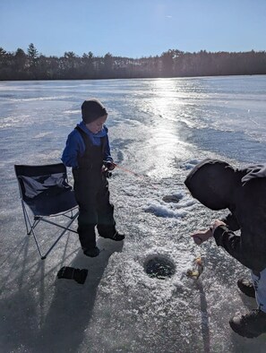 A person standing on a frozen surface with a chair and a bag nearby.