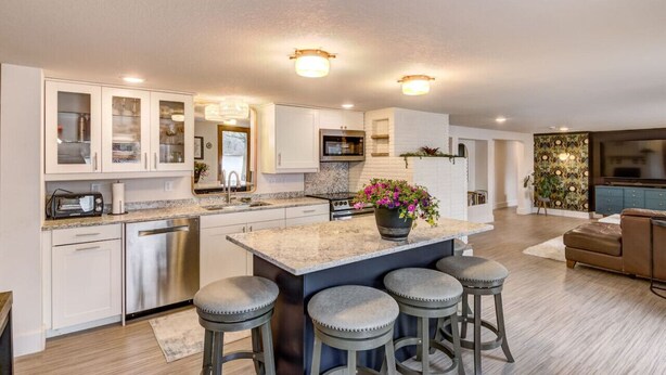 A modern kitchen with a central island, bar stools, stainless steel appliances, and a decorative plant.
