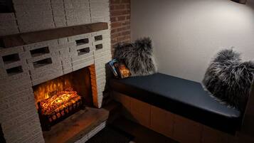 A fireplace with a brick surround, a bench with a fur throw, and a wall-mounted lamp.