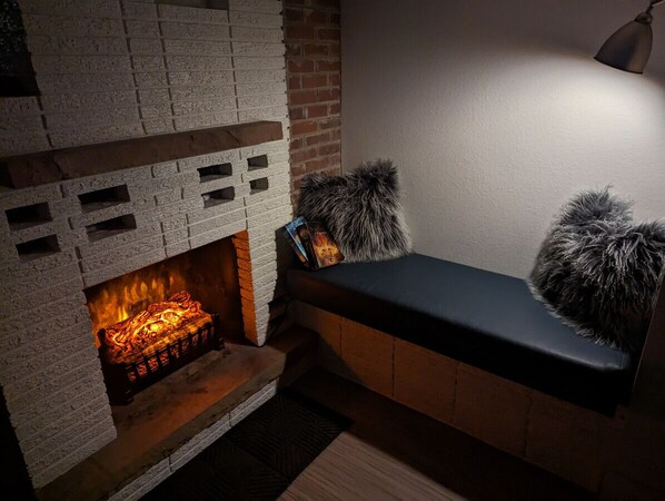 A fireplace with a brick surround, a bench with a fur throw, and a wall-mounted lamp.