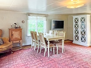 A dining area with a table and chairs, a television mounted on the wall, and a cabinet with decorative items. - 6 Person Holiday Home in Loftahammar (Loftahammar)