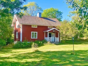 Una casa de madera roja con un porche blanco, rodeada de follaje.