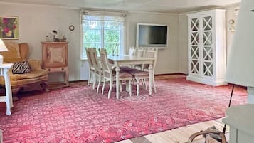 A dining area with a table and chairs, a television mounted on the wall, and a patterned rug on the floor.