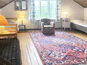 A room with a bed, a chair, a small table, a lamp, and a window with curtains.
