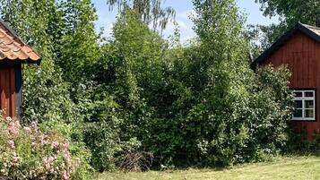 A rustic wooden cabin with a thatched roof, surrounded by dense greenery and flowering bushes.