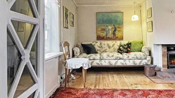 Een woonkamer met een gestreept bankje, een schilderij aan de muur en een open haard.