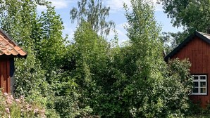 A wooden cabin with a red roof, surrounded by dense greenery and a grassy area. - 6 Person Holiday Home in Loftahammar (Loftahammar)
