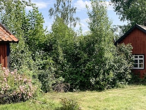 A wooden cabin with a red roof, surrounded by dense greenery and a grassy area. - 6 Person Holiday Home in Loftahammar (Loftahammar)
