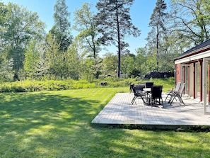 A deck with outdoor furniture, surrounded by a grassy lawn and trees.