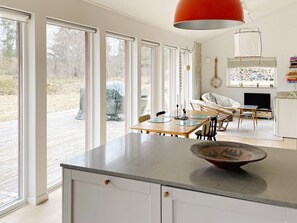 Une cuisine moderne dotée de grandes fenêtres, un coin repas et un espace de vie avec un téléviseur et des livres.
