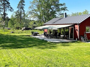 A red building with a covered patio area, outdoor furniture, and a lawn.