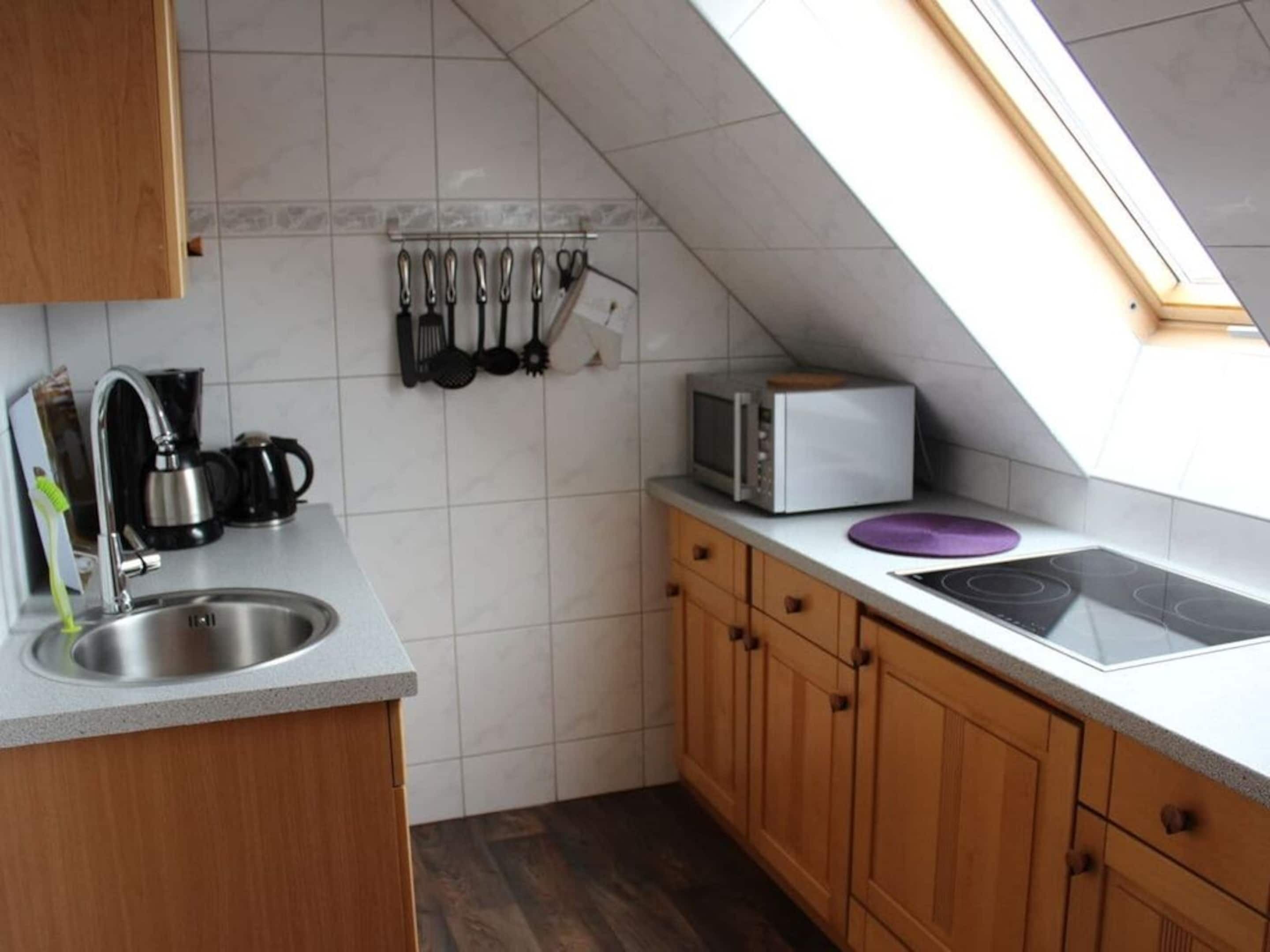 A kitchen with a built-in stove, a microwave, and a coffee maker. There is a set of knives hanging on the wall and a window above the sink.