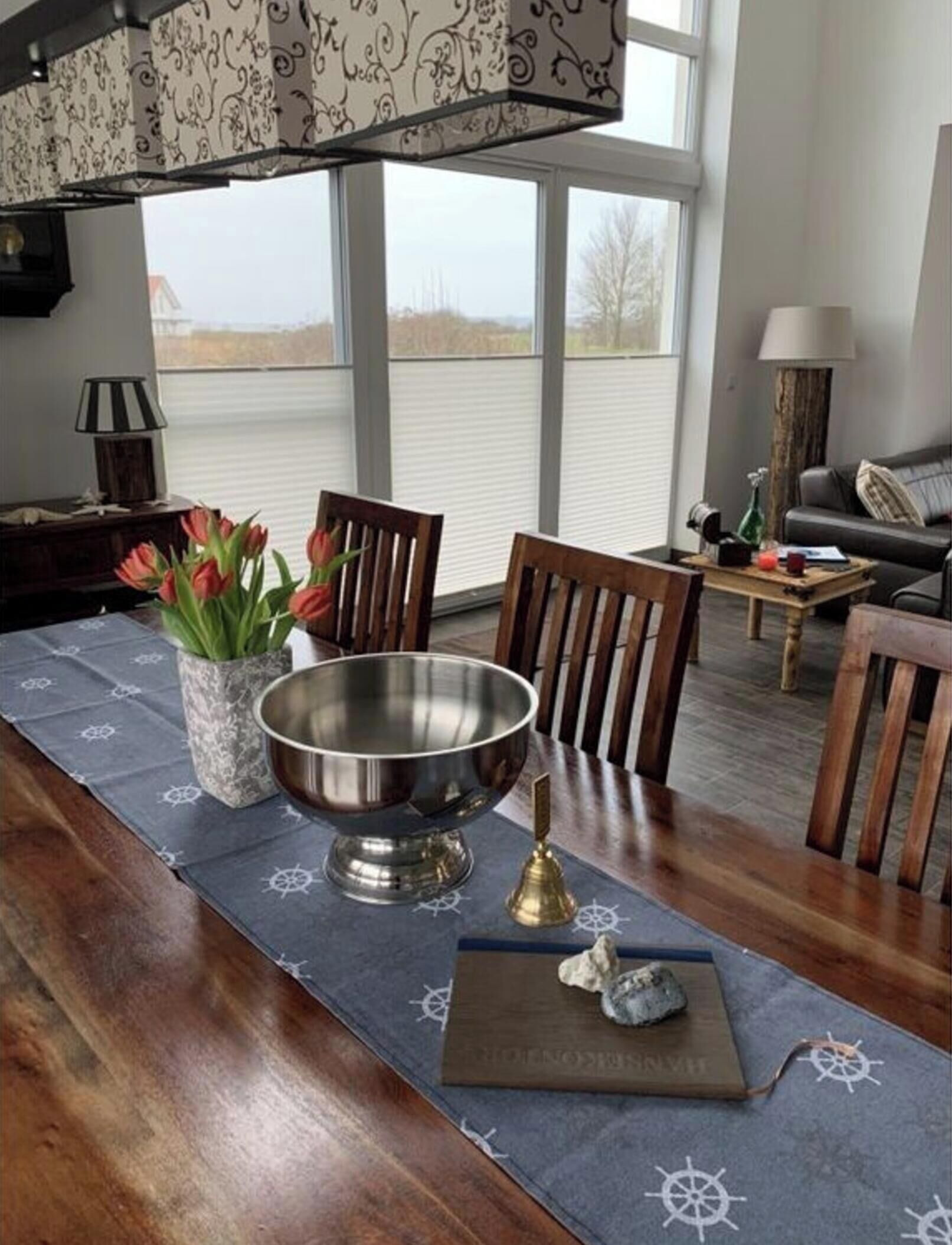 A dining area with a wooden table, a metal bowl, a vase with flowers, and a book with a compass design.